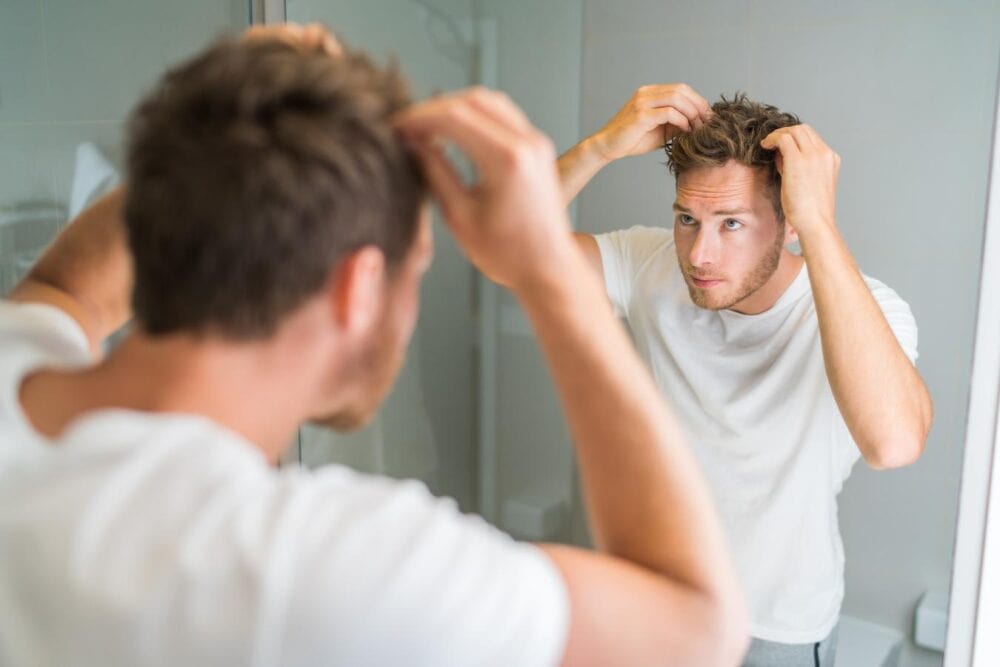 man styling his hair in the mirror hat line